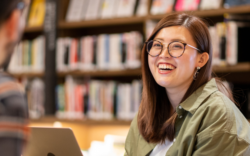 Young woman in a library smiling at someone sat opposite her