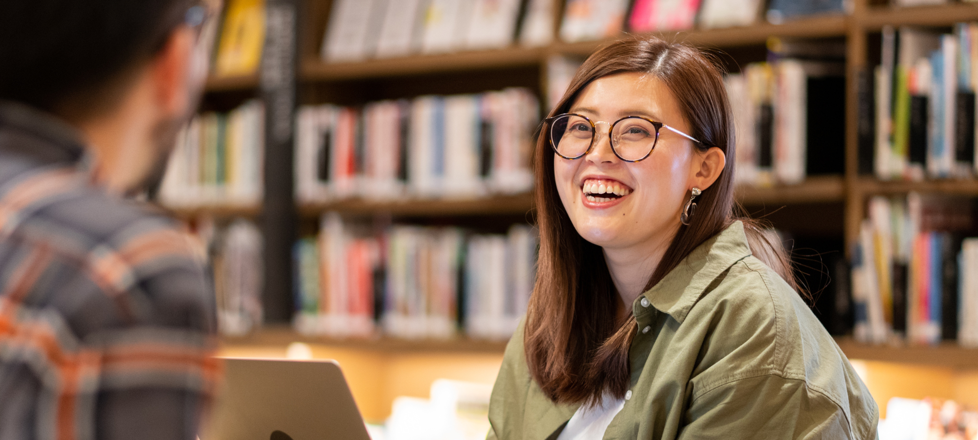 Young woman in a library smiling at someone sat opposite her